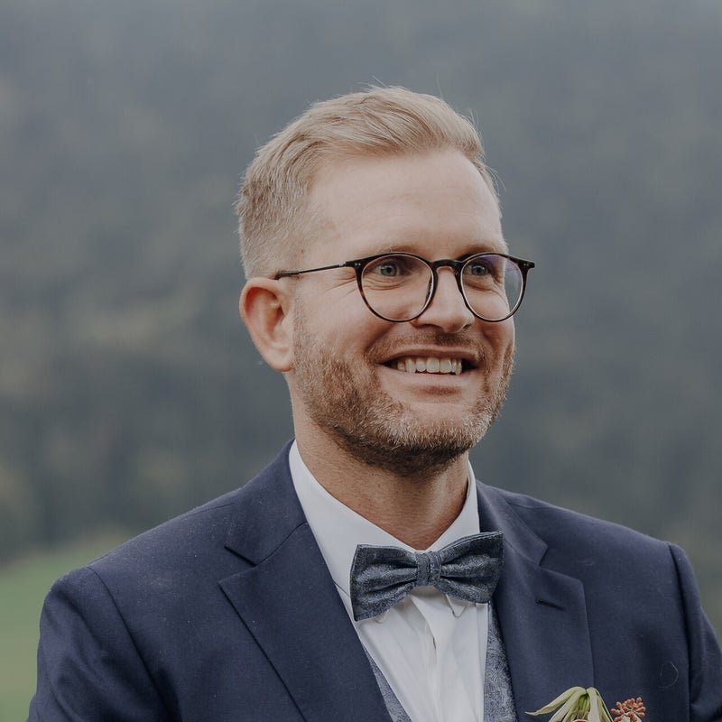 Braut betrachtet ihren Blumenstrauß, Bräutigam im Hintergrund
