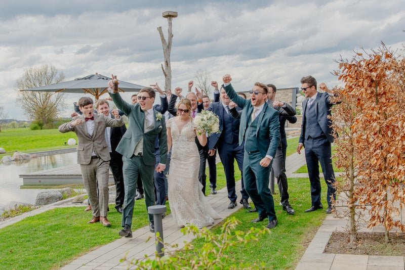 Brautpaar und lachende Gruppe männlicher Gäste feiern ausgelassen die Hochzeit