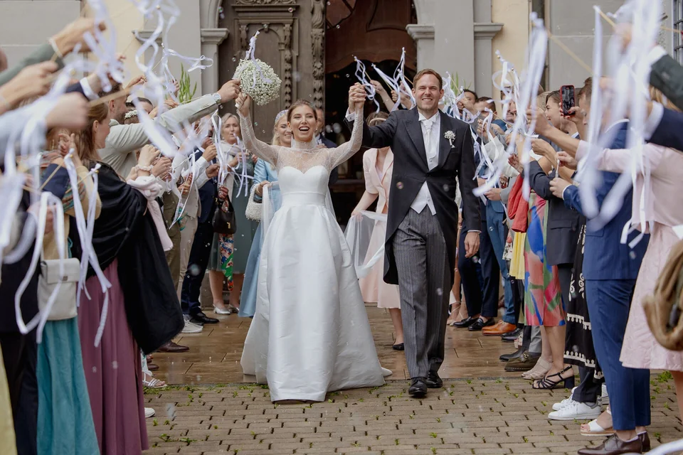 Brautpaar verlässt Kirche nach Trauung, Gäste werfen Konfetti und jubeln, emotionale Hochzeitsmomente, Hochzeitsfotograf René Cerny München